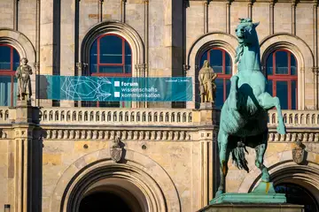 Eingang der Leibniz Universität Hannover. Über dem Eingang hängt ein großes, petrolfarbenes Banner mit dem Logo des FWK.