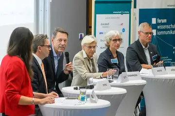 Mehrere Personen stehen hinter Stehtischen nebeneinander und diskutieren.