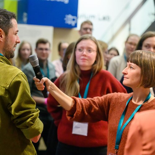 Zwei Personen beim Interview, weitere Personen im Hintergrund.