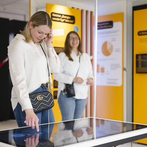 Zwei Personen bedienen Touchscreen in hellem und bunten Ausstellungsraum