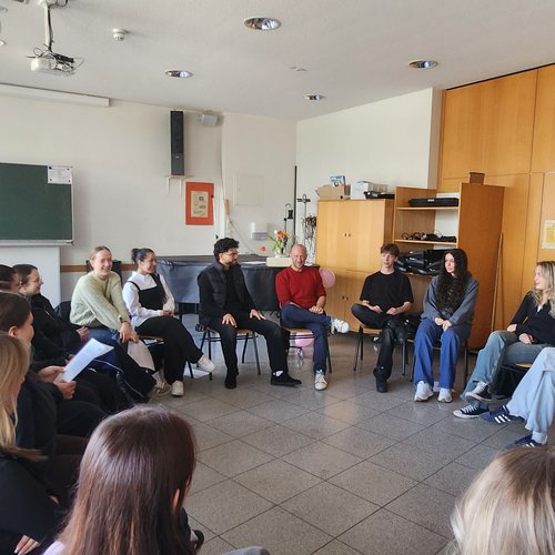 Personen sitzen in einem Klassenraum im Kreis und unterhalten sich angeregt.