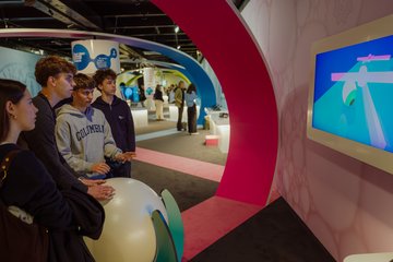 Blick in die Ausstellung auf der MS Wissenschaft zum Thema Medizin der Zukunft, im Vordergrund Schüler:innen an einem Exponat zur Entwicklung von Kontaktlinsen.