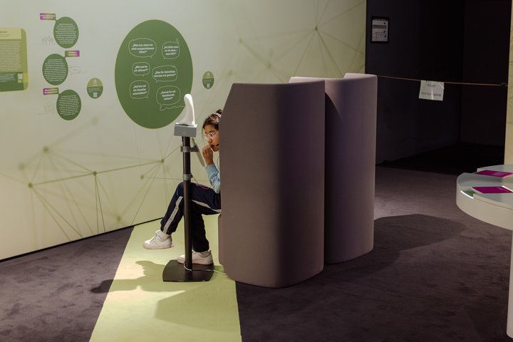 Ausstellung auf der MS Wissenschaft zum Thema Medizin des Zukunft, Exponat Elderbot, eine Person sitzt einem Sessel und spricht in ein Mikrofon