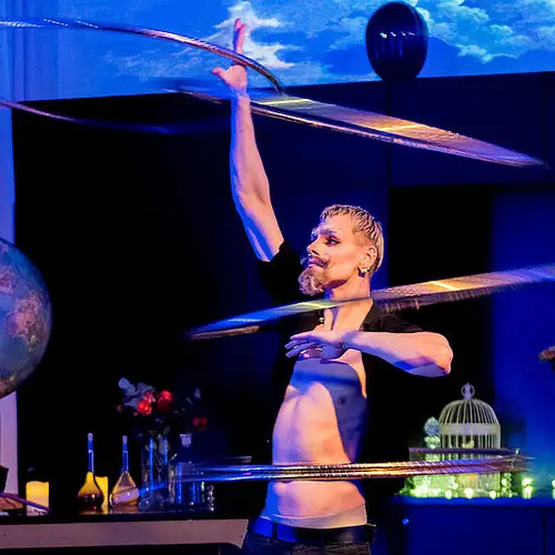 Foto vom Wissenschaftsvarieté Glitzern und Denken. Ein Darsteller balanciert mit Hula Hoop-Ringen. Im Hintergrund sind unter anderem ein Globus und Reagenzgläser zu sehen.