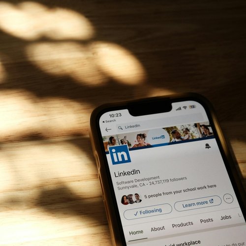 Smartphone mit LinkedIn-App liegt auf Tisch, der von Sonne angestrahlt wird