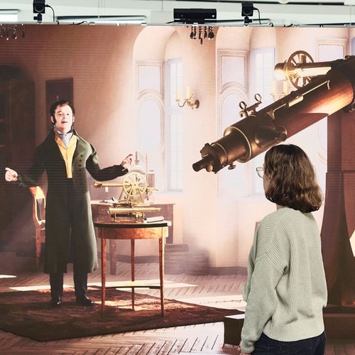 Digitale Projektion von Joseph von Fraunhofer, der mit einer Person vor dem Display interagiert