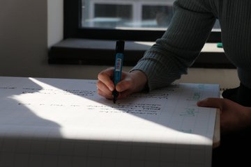 Mit einem Textmarker in der Hand ist hier ein Arm gezeigt, der den Stift auf einem Plakat ansetzt.