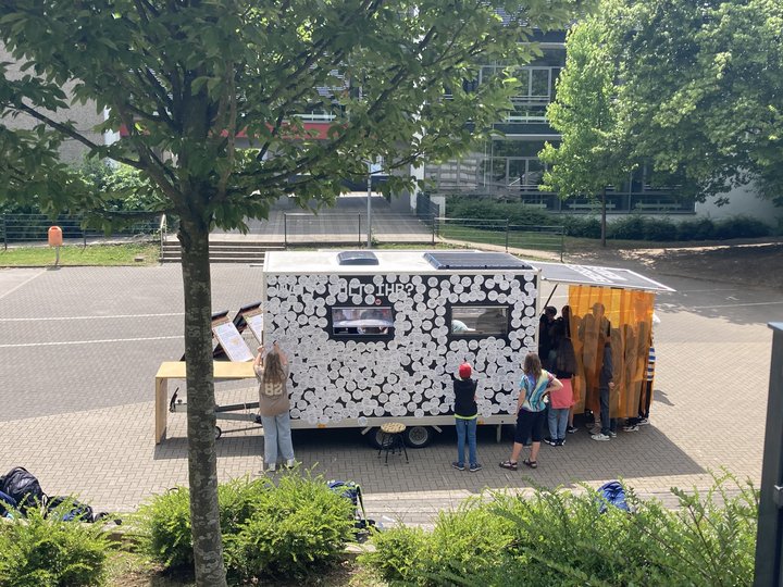 Foto des Energiemobils auf einem Parkplatz, Jugendliche stehen vor einer mit Sticker beklebten Seite des Energiemobils