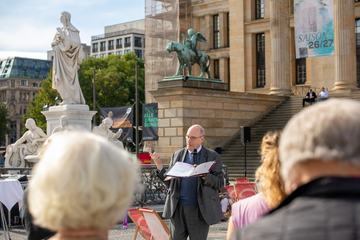 Christoph Markschies begrüßt auf Gendarmenmarkt neben Statue von Schiller