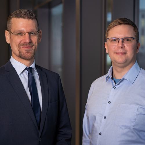 Teamfoto von Damian Groten und Florian Rummler. Beide lächeln freundlich in die Kamera. Damian Groten trägt einen Anzug und Krawatte. Florian Rummler trägt ein Hemd.