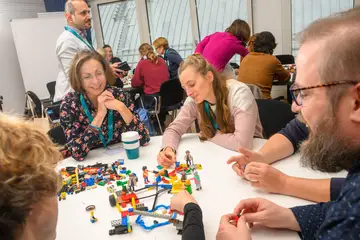 Personen sitzen zusammen an einem Tisch und bauen etwas mit Legosteinen.