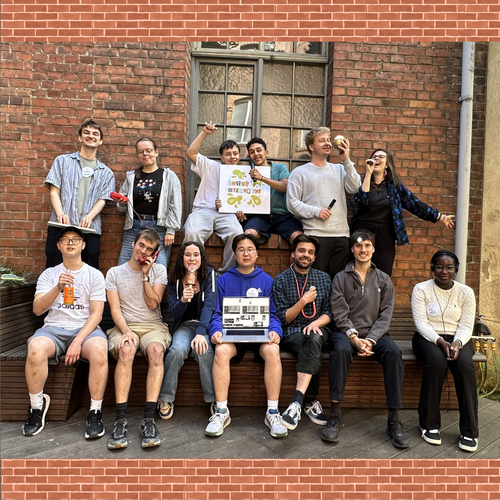 Eine Gruppe von Jugendlichen und Projektmitarbeiter*innen von Make Your School sitzt fröhlich für ein Bild zusammen vor einer braunen Backsteinmauer.