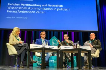 4 Personen auf Bühne sitzend vor Leinwand