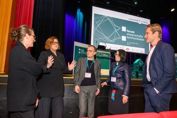 5 Personen stehen vor einer Bühne und diskutieren