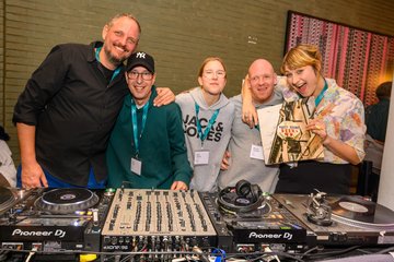 5 Personen stehen Arm in Arm hinter DJ-Pult