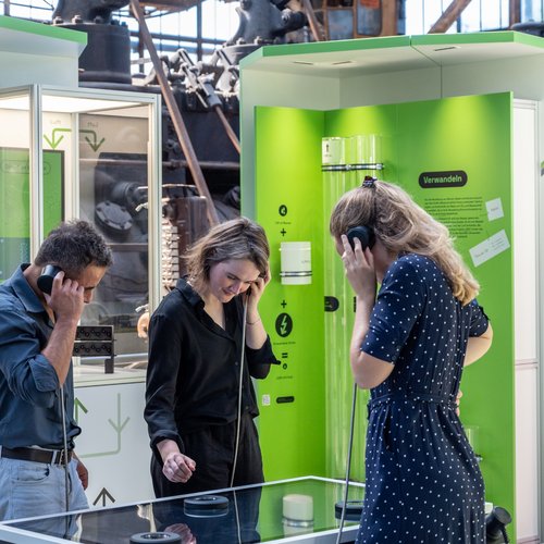 Mehrere Personen betrachten ein Exponat und tragen Kopfhörer