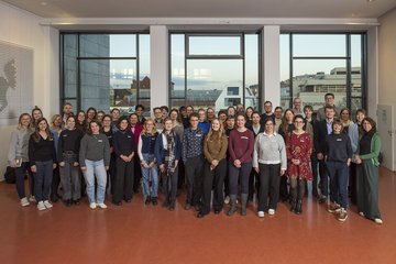 Eine große Gruppe von Menschen in bunter Kleidung steht für ein Gruppenfoto zusammen.