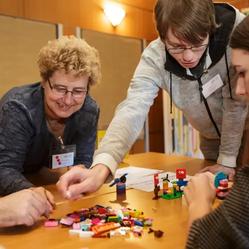 Schüler*innen und eine Forscherin basteln gemeinsam an einem Tisch mit Legosteinen.
