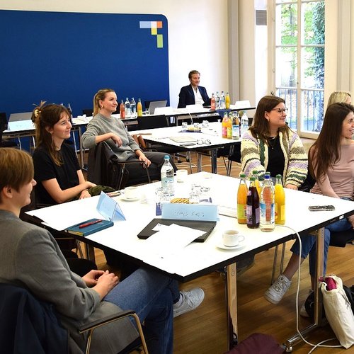 Personengruppe sitzend um Tische in Seminarraum, schauen alle in eine Richtung