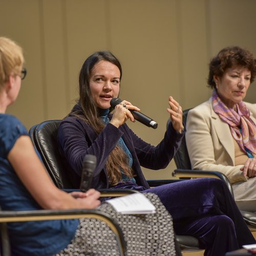 Drei Frauen sitzen nebeneinander, die Frau in der Mitte spricht in ein Mikrofon.