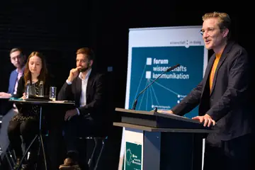 Benedikt Fecher steht auf der Bühne an einem Redepult und hält eine Rede.