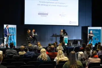 Ein voller Hörsaal. Auf der Bühne diskutieren mehrere Personen
