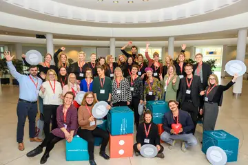 Das WiD-Team steht als Gruppe zusammen. Einige Personen reißen ihre Hände in die Höhe oder halten WiD-Sitzkissen in der Hand.