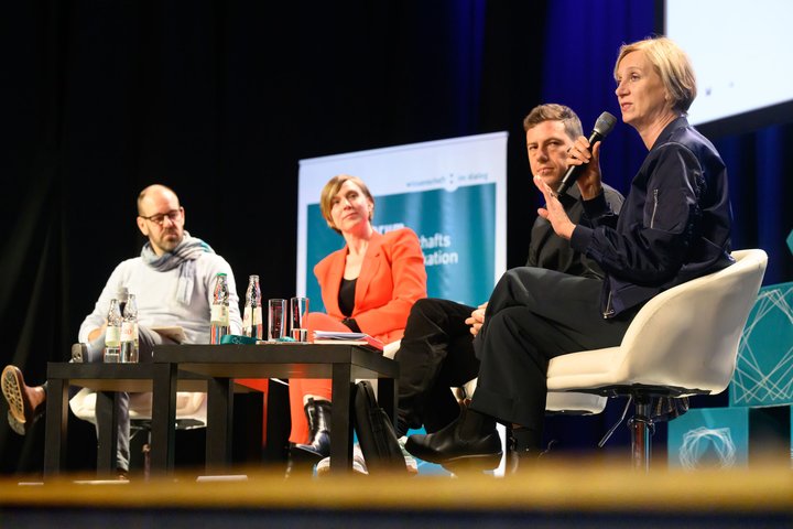 Vier Personen sitzen auf dem Podium zusammen und diskutieren.